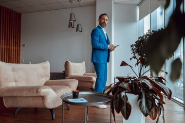 Modern lobide duran akıllı telefonlu mutlu şık adam.