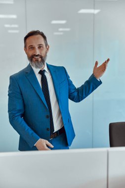 Gülen adam elleriyle boş duvarda bir şey gösteriyor.