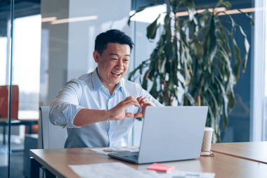 Modern ofiste öğle yemeği arasında arkadaşlarıyla görüntülü iletişim kuran mutlu Asyalı adam.