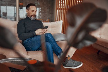 Ofis lobisinde telefonla mesaj yazan sakallı bir adam.