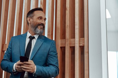 Mutlu beyaz adam telefon ile ofis alanına bakıyor.