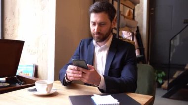 Süitteki yakışıklı beyaz adam kafedeki akıllı telefondan mesaj atıyor. İş adamı sohbeti..