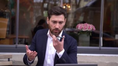 Handsome elegant Caucasian man sending voice message with smartphone. Talk via speakerphone.