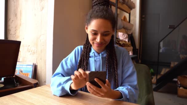 Całkiem szczęśliwa młoda kobieta siedząca w kawiarni z telefonem komórkowym. Kobieta przewijanie na smartfonie. — Wideo stockowe