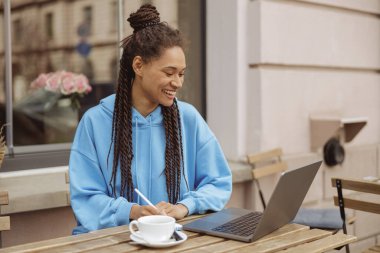Dizüstü bilgisayarla konuşan ve not alan genç ve şık bir kadın. Kafe terasında. Serbest Çalışan.