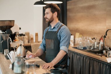 Kafeteryada çalışan yakışıklı erkek barista ve müşterilerden sipariş alıyor.