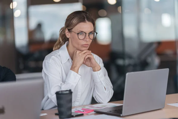 Serious businesswoman with glasses working on laptop at workplace in modern office — 스톡 사진