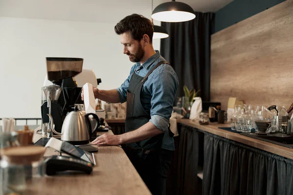 Kahveci kahve makinesinin kahve makinesinin tankına kahve çekirdeği doldurur.