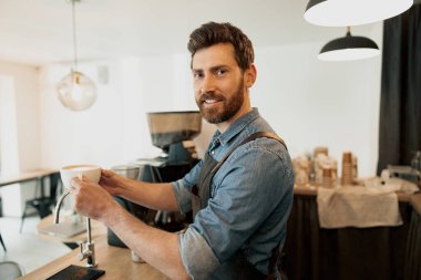 Elinde kahve fincanı tutan yakışıklı barista ve kameraya bak.