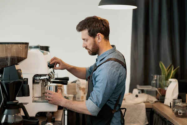 Adam barista sütü sürahide makinenin buharıyla çırpıyor.