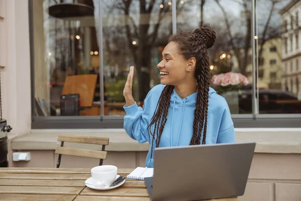 Kahvesinde kahveyle kafede oturan ve el sallayan oldukça neşeli genç bir kadın..