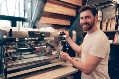 Neşeli, beyaz, yakışıklı, kahve makinesi reklamında kahve hazırlayan kameraya gülümseyen adam..