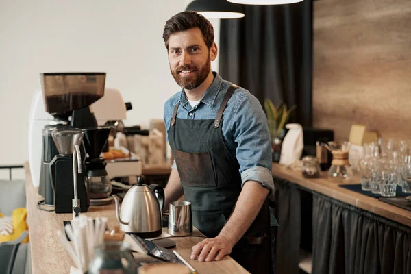 Kahve dükkanında tezgahın arkasında gülümseyen şık sakallı barista.