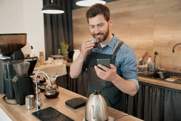 Kahve içen yakışıklı barista öğle yemeği boyunca sosyal medyada geziniyor.