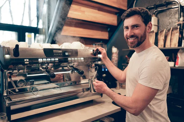 Neşeli, beyaz, yakışıklı, kahve makinesi reklamında kahve hazırlayan kameraya gülümseyen adam..