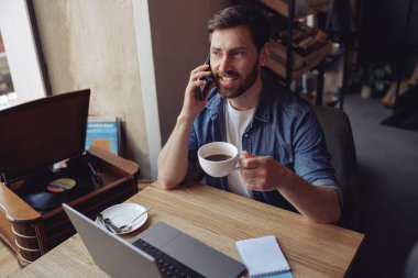 Çekici beyaz adam cep telefonuyla konuşuyor ve kafede kahve içiyor. İş sohbeti.