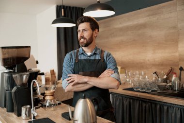 Yakışıklı, genç kahve dükkanı sahibi tezgahın arkasında duruyor ve başka tarafa bakıyor.