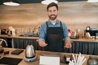 Barista tezgahın arkasında duran sadık bir müşteriyi sevinçle selamlıyor.