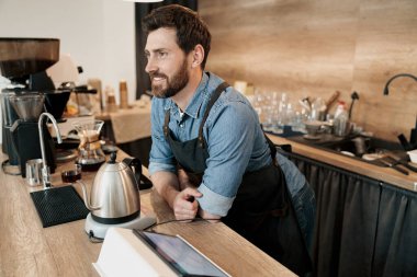Modern tavan arası kafede müşterileri bekleyen yakışıklı, gülümseyen bir barista.