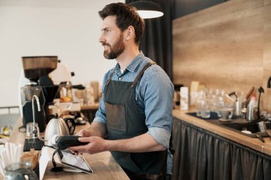 Gülümseyen barmen elinde bir ödeme terminali tutuyor ve müşteriye bakıyor.