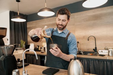 Tarz sahibi sakallı, önlüklü, gülümseyen barista bardağa filtre kahve doldurdu.