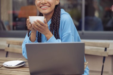 Melez, genç ve şık bir bayanın ellerinde bir fincan kahve. Kafe açık havada. Dizüstü bilgisayarda serbest çalışan.
