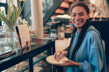 Neşeli, genç Stylsih karışık ırktan bayan barmen tezgahta bir parça kek tutuyor..