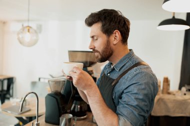 Handsome barista with stylish beard smelling coffee in cafeteria