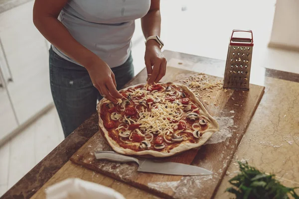 The process of cooking pizza with mushrooms and grated cheese on a wooden board