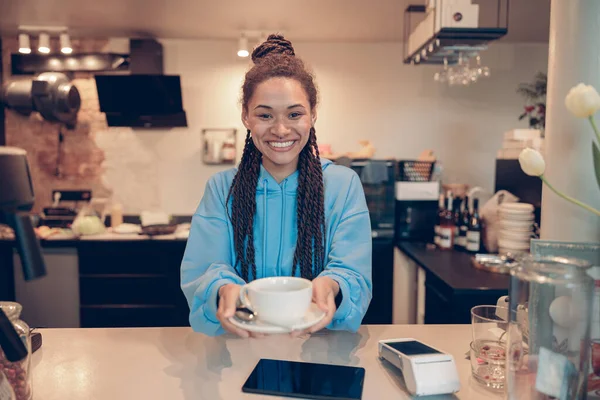 Saçları örgü örüp kameraya kahve dağıtan oldukça genç, melez bir bayan barista..