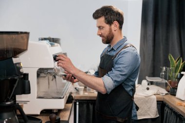 Barista kahve makinesini yıkıyor ve elinde bir kahve tankı tutuyor.