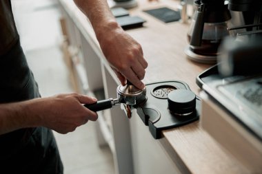 Close up of barista man hands is holding portafilter and coffee tamper