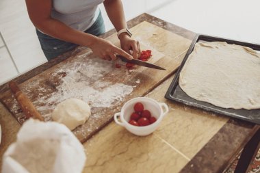 Mutfakta bir ev hanımı pizza pişirmek için ahşap bir tahtada domates kesiyor.