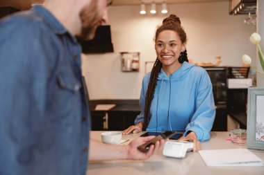 Erkek müşterinin kahvenin parasını akıllı telefon ödeme servisiyle ödemesi. Tezgahtaki garson..