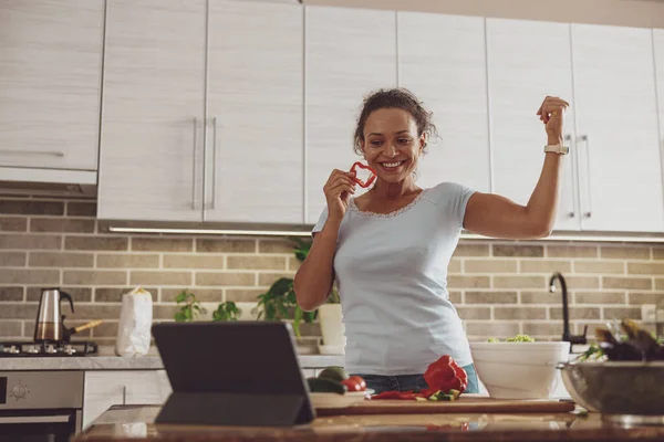 A woman prepares a vegetable salad in the kitchen and shows her biceps