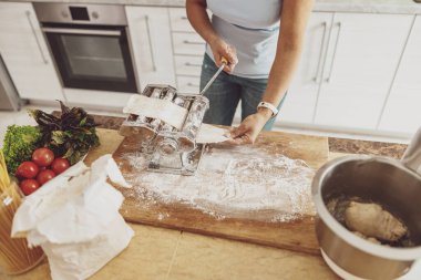 A woman standing at the kitchen table cuts noodles in a noodle cutter