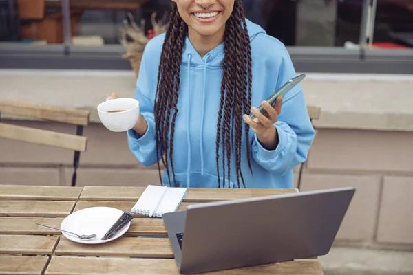 Kafeteryadaki masada dizüstü bilgisayarda kahve ve cep telefonuyla mutlu kadın elleri..