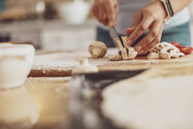 Mutfağın arka planında tahta bir tahtada ev yapımı pizza için mantar dilimlemek.