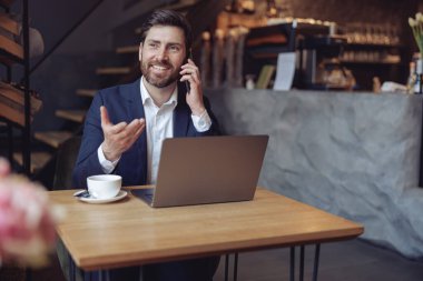 Çekici, genç, zarif iş adamı kafede dizüstü bilgisayarla konuşuyor ve gülümsüyor. Konuşma.