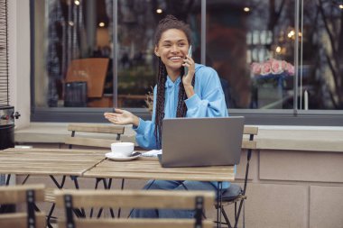 Çekici, neşeli genç bayan kafede kahve içerken cep telefonuyla konuşuyor..