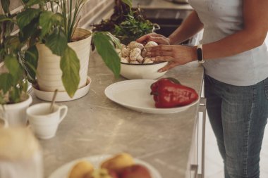 Bir kadının elleri mutfak masasındaki bir tabak mantarın üzerinde uzanır..
