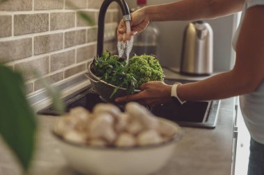 Bir kadının elleri bir kase yeşilliği su altında tutar..