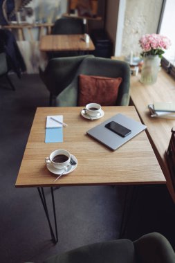 Masanın üstünden beyaz kahve fincanları ve iş malzemeleriyle manzarayı seyret. Laptop ve telefon.