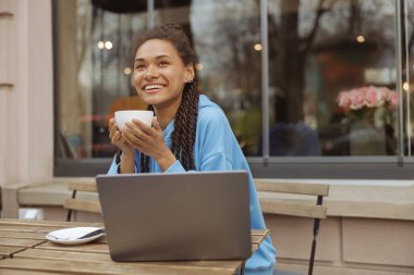 Güzel, genç, melez, stil sahibi bir kadın. Elinde piercing, elinde kahve, hayal kuruyor, gülümsüyor..