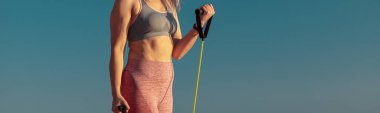 Spor sahasında spor giyinen güçlü bir kadın fitness direnci bantları kullanıyor.