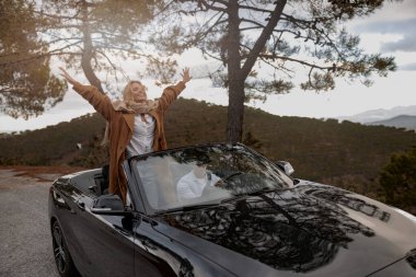 Neşeli Kafkasyalı güzel kadın üstü açık arabada ellerini havaya kaldırdı.