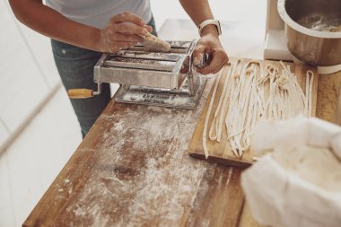 Mutfağın arka planında makarna keskisi olan bir kadın tarafından yapılan ev yapımı erişteler.