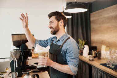 Barista hazır kahve filtresi tutarken sadık bir müşteriyi sevinçle selamlıyor. 