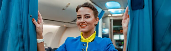 Wesoła Stewardessa Mundurze Stewardessy Patrzy Kamerę Uśmiecha Się Trzymając Zasłony — Zdjęcie stockowe