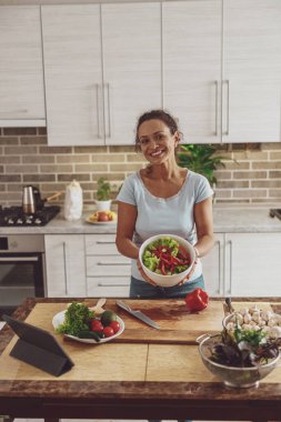 Mutfakta dikilen bir kadın elinde doğranmış sebzelerle dolu bir konteynır tutuyor.